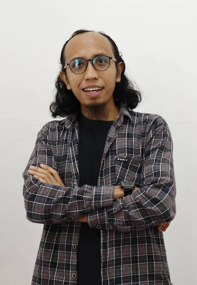 Ali Mashuri smiling in a grey plaid shirt and glasses